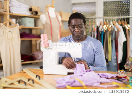 African American man tailor sews clothes in sewing machine. African American man tailor sews clothes in sewing machine. 138915980