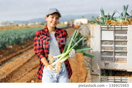 Positive girl farmer holding harvested leeks on field Positive girl farmer holding harvested leeks on field 138915983