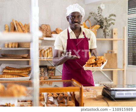 African male baker worker sells croissants, shows many products African male baker worker sells croissants, shows many products 138915989