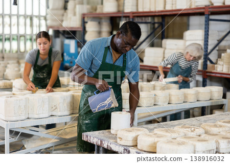 Slip casting - african american worker pours slip mass from jug into plaster mold in pottery factory Slip casting - african american worker pours slip mass from jug into plaster mold in pottery factory 138916032