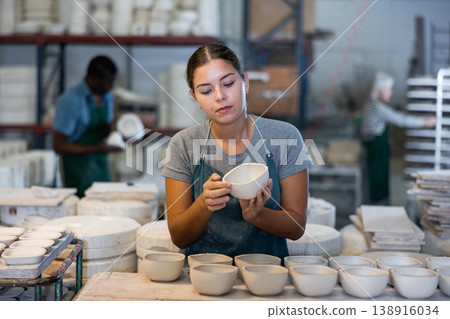 Young woman checks quality of pottery after being removed from plaster mold Young woman checks quality of pottery after being removed from plaster mold 138916034