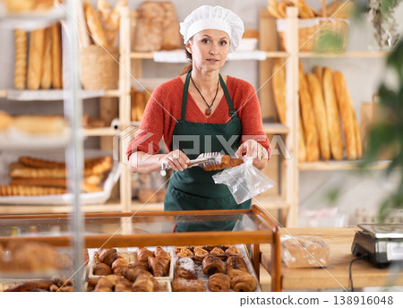 European woman vendor sells sweet puff pastry and puts croissant in plastic disposable bag European woman vendor sells sweet puff pastry and puts croissant in plastic disposable bag 138916048