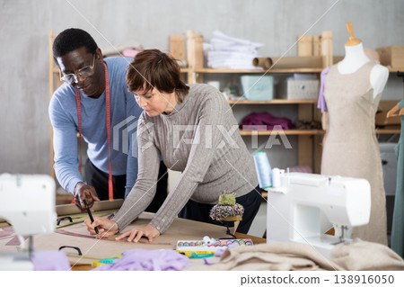 Woman tailor and African man companion draw dress pattern of product on paper Woman tailor and African man companion draw dress pattern of product on paper 138916050