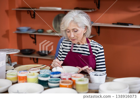 Mature craftswoman painting clay plates acrylic paints in art studio 138916073