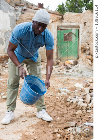 Upset afro american man observing the destruction of his home Upset afro american man observing the destruction of his home 138916114