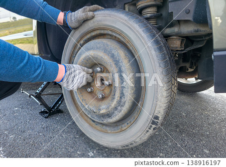 A young man tightens the bolts on a spare tire after an emergency tire change. High quality photo A young man tightens the bolts on a spare tire after an emergency tire change. High quality photo 138916197