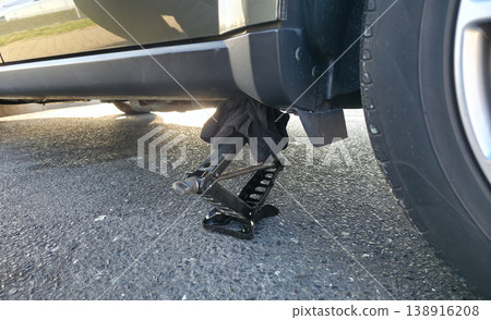 A hand-held portable jack is installed under a car to lift the vehicle for changing a tire. High quality photo A hand-held portable jack is installed under a car to lift the vehicle for changing a tire. High quality photo 138916208