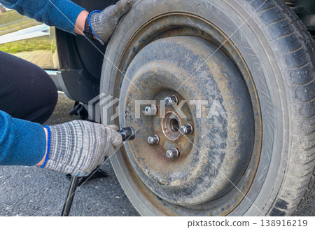 A young man tightens the bolts on a spare tire after an emergency tire change. High quality photo A young man tightens the bolts on a spare tire after an emergency tire change. High quality photo 138916219