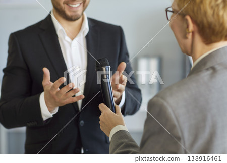 Reporter handing microphone to business speaker during interview in modern office 138916461