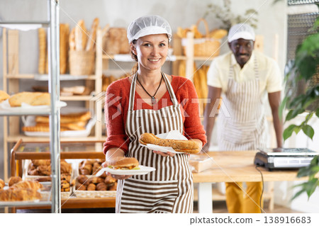 Woman entrepreneur, owner of bakery, holds out sandwich in disposable dish plate in hand Woman entrepreneur, owner of bakery, holds out sandwich in disposable dish plate in hand 138916683