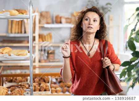 European woman near window of bakery food court store examines assortment 138916687