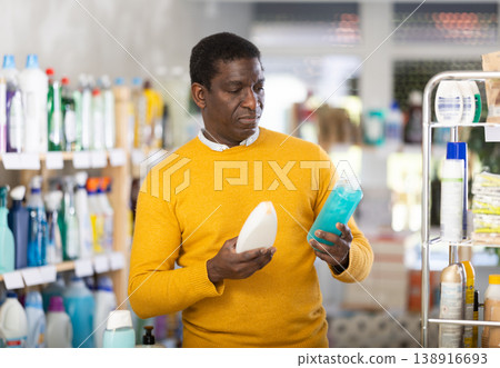 Male buyer chooses shampoo or shower gel in household goods department of supermarket Male buyer chooses shampoo or shower gel in household goods department of supermarket 138916693