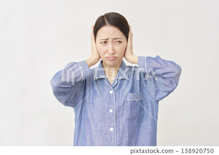 Woman in pajamas covering her ears white background 138920750