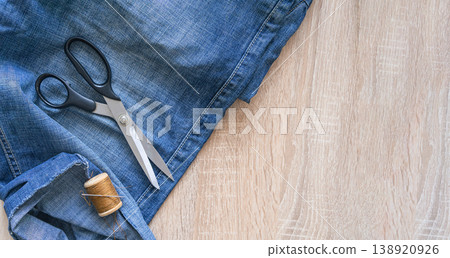 Sewing tools and brown thread on blue denim for mending, tailoring and upcycling old jeans, diy repair, craft and sustainable fashion project. Tailoring blue denim jeans with scissors and thread 138920926