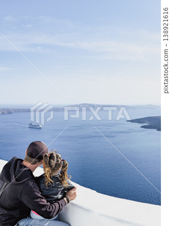 Heartwarming Santorini moment with father and daughter on a terrace, embracing gently while gazing at the endless Aegean Sea and distant islands Heartwarming Santorini moment with father and daughter on a terrace, embracing gently while gazing at the endless Aegean Sea and distant islands 138921616