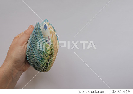 Female hand tightly squeezing a huge thick stack of 20 Euro banknotes folded in half. High-volume cash concept on a white background with a large copy space Female hand tightly squeezing a huge thick stack of 20 Euro banknotes folded in half. High-volume cash concept on a white background with a large copy space 138921649