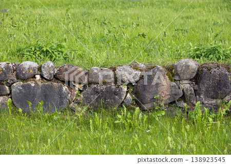 A low rustic stone wall covered in moss sits amid a vibrant green meadow 138923545