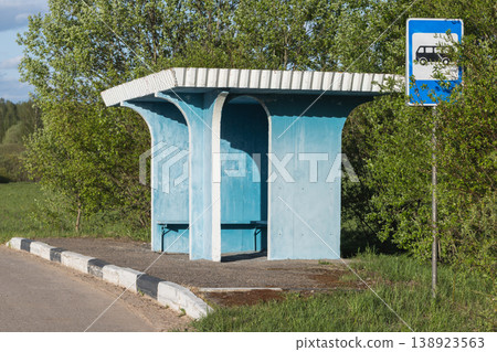 A weathered blue bus stop shelter sits empty beside a quiet country road 138923563