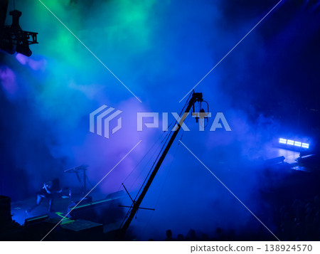 Dynamic concert stage with performer silhouette, dramatic blue and green smoke, and a camera crane capturing the electrifying live music production Dynamic concert stage with performer silhouette, dramatic blue and green smoke, and a camera crane capturing the electrifying live music production 138924570