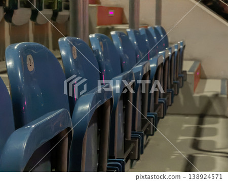 Row of empty blue numbered stadium seats waiting for an audience at a large sports arena or entertainment venue, depicting solitude before a gathering Row of empty blue numbered stadium seats waiting for an audience at a large sports arena or entertainment venue, depicting solitude before a gathering 138924571