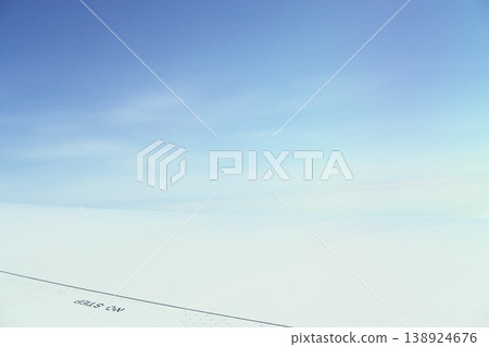 A calm blue sky and the tip of a wing, with contrails in the background. 138924676