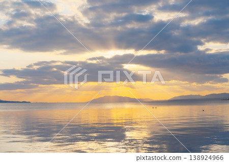 The calm surface of the lake at dusk, the distant mountain range, and the clouds floating in the sky. 138924966