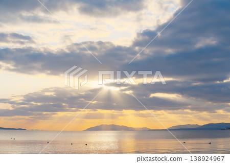 The calm surface of the lake at dusk, the distant mountain range, and the clouds floating in the sky. 138924967