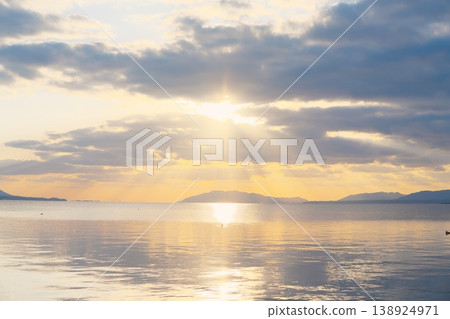 The calm surface of the lake at dusk, the distant mountain range, and the clouds floating in the sky. The calm surface of the lake at dusk, the distant mountain range, and the clouds floating in the sky. 138924971