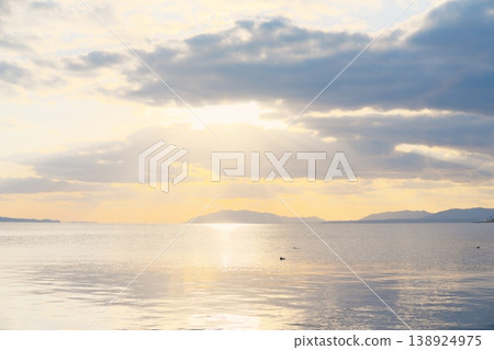 The calm surface of the lake at dusk, the distant mountain range, and the clouds floating in the sky. The calm surface of the lake at dusk, the distant mountain range, and the clouds floating in the sky. 138924975