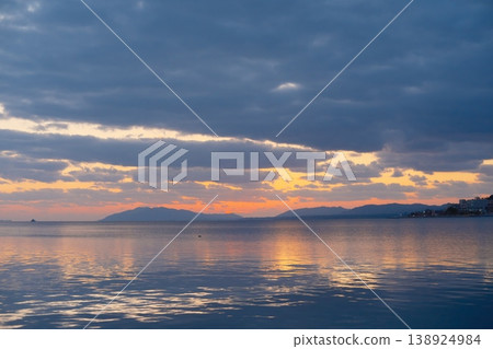 The sun sinking into the azure lake, its orange light trails reflected on the water's surface. The sun sinking into the azure lake, its orange light trails reflected on the water's surface. 138924984