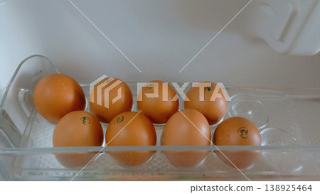 Eight brown chicken eggs with blue quality stamps arranged in a clear plastic refrigerator door shelf. Eight brown chicken eggs with blue quality stamps arranged in a clear plastic refrigerator door shelf. 138925464