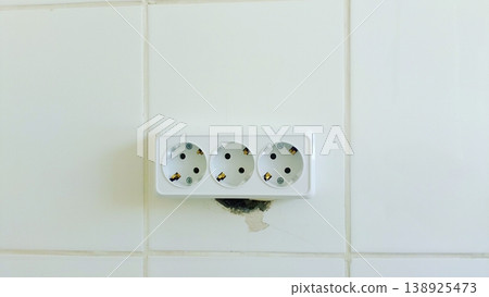 White triple electrical wall socket mounted on a clean white tiled wall. Minimalist interior detail showing home utility and power supply. White triple electrical wall socket mounted on a clean white tiled wall. Minimalist interior detail showing home utility and power supply. 138925473