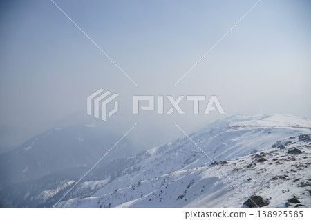 Mountain range covered in snow with a hazy sky in the background Mountain range covered in snow with a hazy sky in the background 138925585