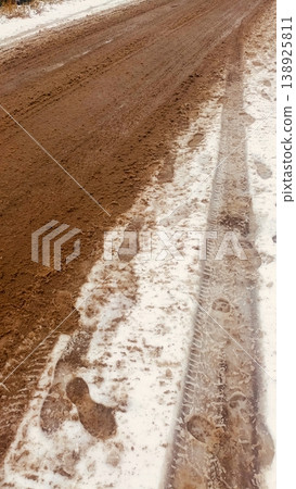 A textured view of a muddy dirt road partially covered with slushy white snow, tire tracks, and footprints. A textured view of a muddy dirt road partially covered with slushy white snow, tire tracks, and footprints. 138925811