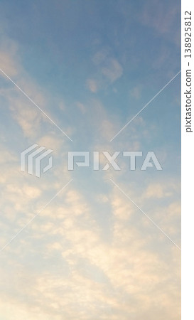 Soft altocumulus clouds scattered across a pale blue sky during a warm golden hour sunset. 138925812