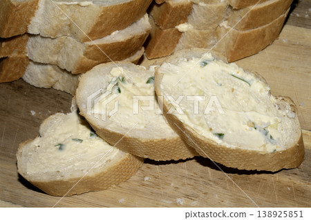 Fresh cut baguette bread in slices with herb garlic butter on a wooden background Fresh cut baguette bread in slices with herb garlic butter on a wooden background 138925851