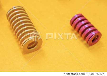 Group of yellow and red industrial compression die springs on a matching yellow background. 138926474