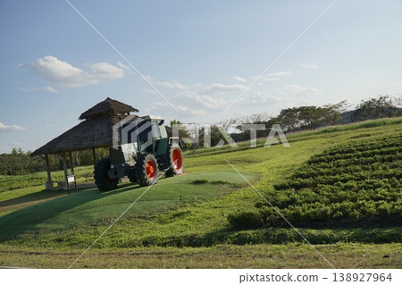Tractor is driving down a field with a green hill in the background 138927964