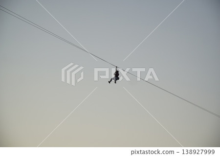 Man is zipping through the air on a zip line Man is zipping through the air on a zip line 138927999