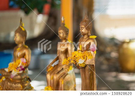 Serene Golden Buddha Statues Surrounded by Colorful Flower Petals in Tranquil Outdoor Setting with Soft Natural Light Serene Golden Buddha Statues Surrounded by Colorful Flower Petals in Tranquil Outdoor Setting with Soft Natural Light 138928620