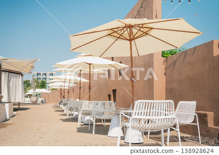 Stylish Outdoor Seating Area with White Umbrellas and Modern Furniture Against a Clear Sky in a Relaxing Atmosphere Stylish Outdoor Seating Area with White Umbrellas and Modern Furniture Against a Clear Sky in a Relaxing Atmosphere 138928624
