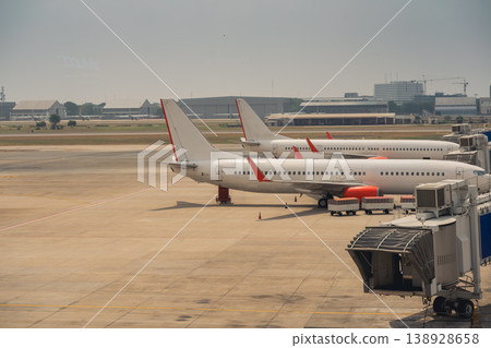 Three Commercial Airplanes Parked at a Modern Airport Terminal Under Clear Sky with Industrial Buildings in Background Three Commercial Airplanes Parked at a Modern Airport Terminal Under Clear Sky with Industrial Buildings in Background 138928658