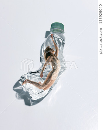 Woman stretching inside crushed plastic bottle symbolizing fight for freedom and movement. 138929040