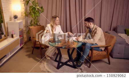 Mental coach consulting client at table with laptop in cozy therapy space. 138929062