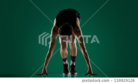 Male athlete bent over in start stance with both hands on floor in studio. Male athlete bent over in start stance with both hands on floor in studio. 138929126