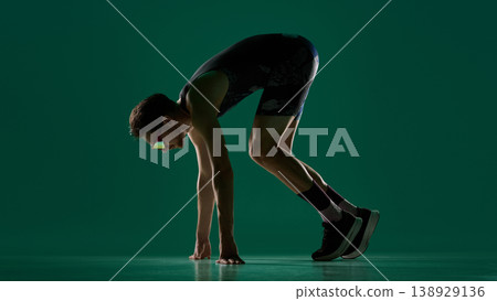 Male athlete in sprint start position viewed from side on green studio background 138929136