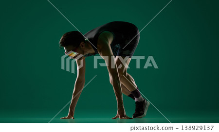Male athlete in starting stance with hands on floor ready to sprint in studio. 138929137