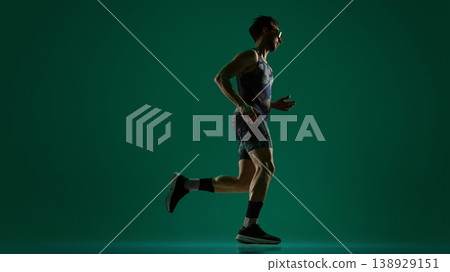 Male athlete captured mid stride running in side view on dark green background Male athlete captured mid stride running in side view on dark green background 138929151