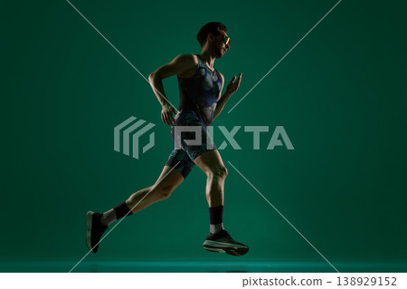Male athlete running in side view full body motion on dark green background. Male athlete running in side view full body motion on dark green background. 138929152