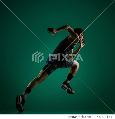 Male athlete accelerating forward in dynamic running pose on dark green. 138929155